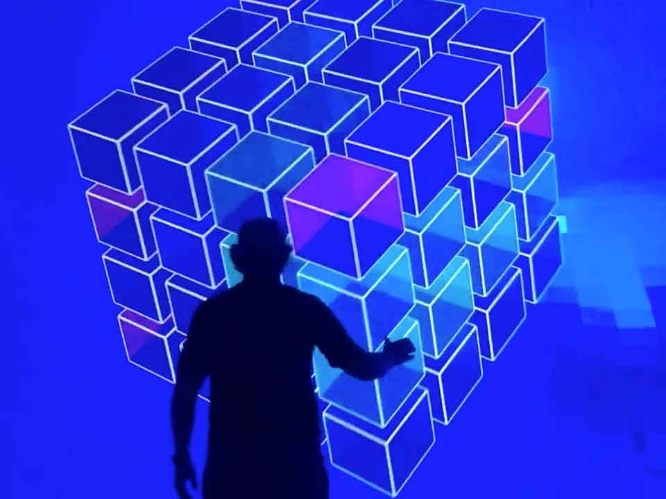 A silhouetted performer reaching toward a projected wall of glowing 3D cubes
